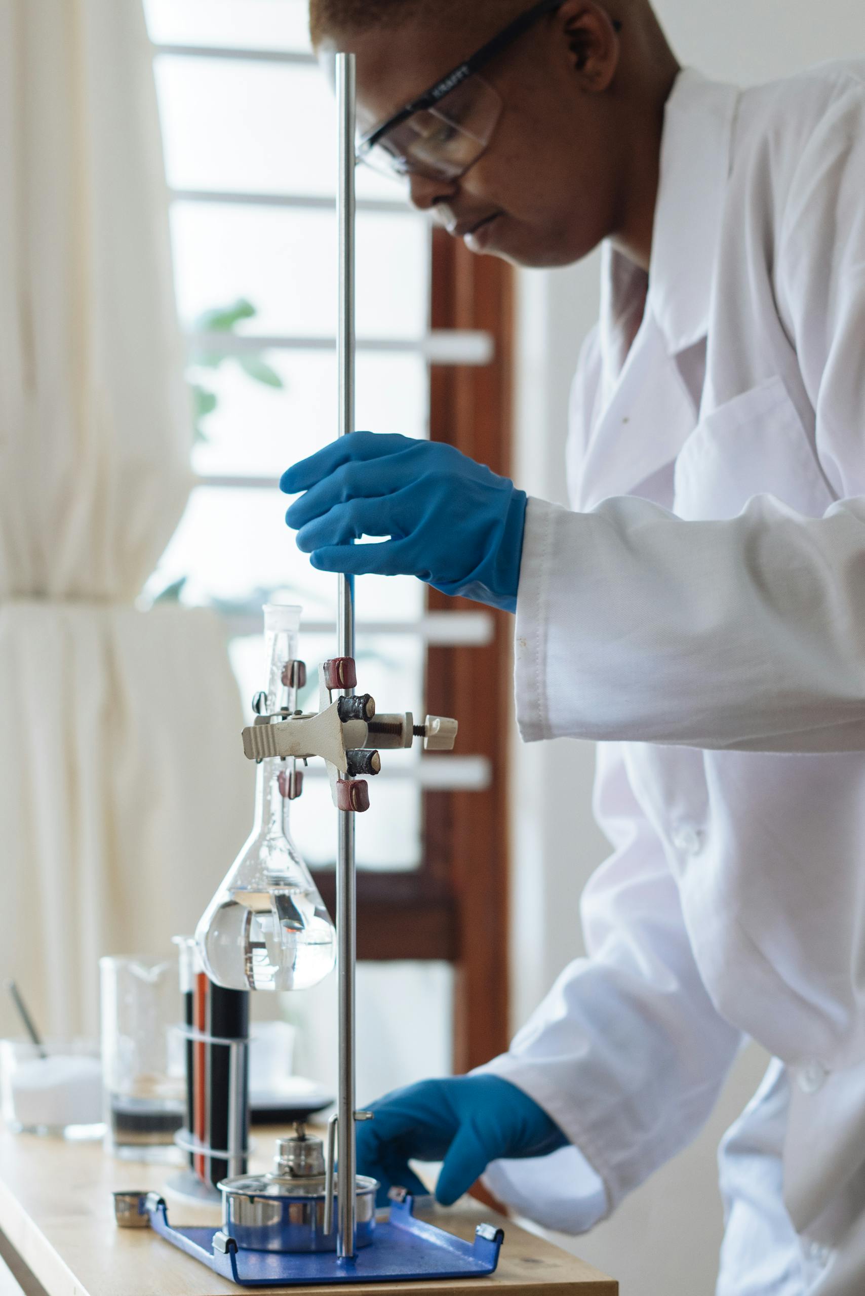 Professional scientist wearing a lab coat and gloves conducting an experiment with glassware indoors.